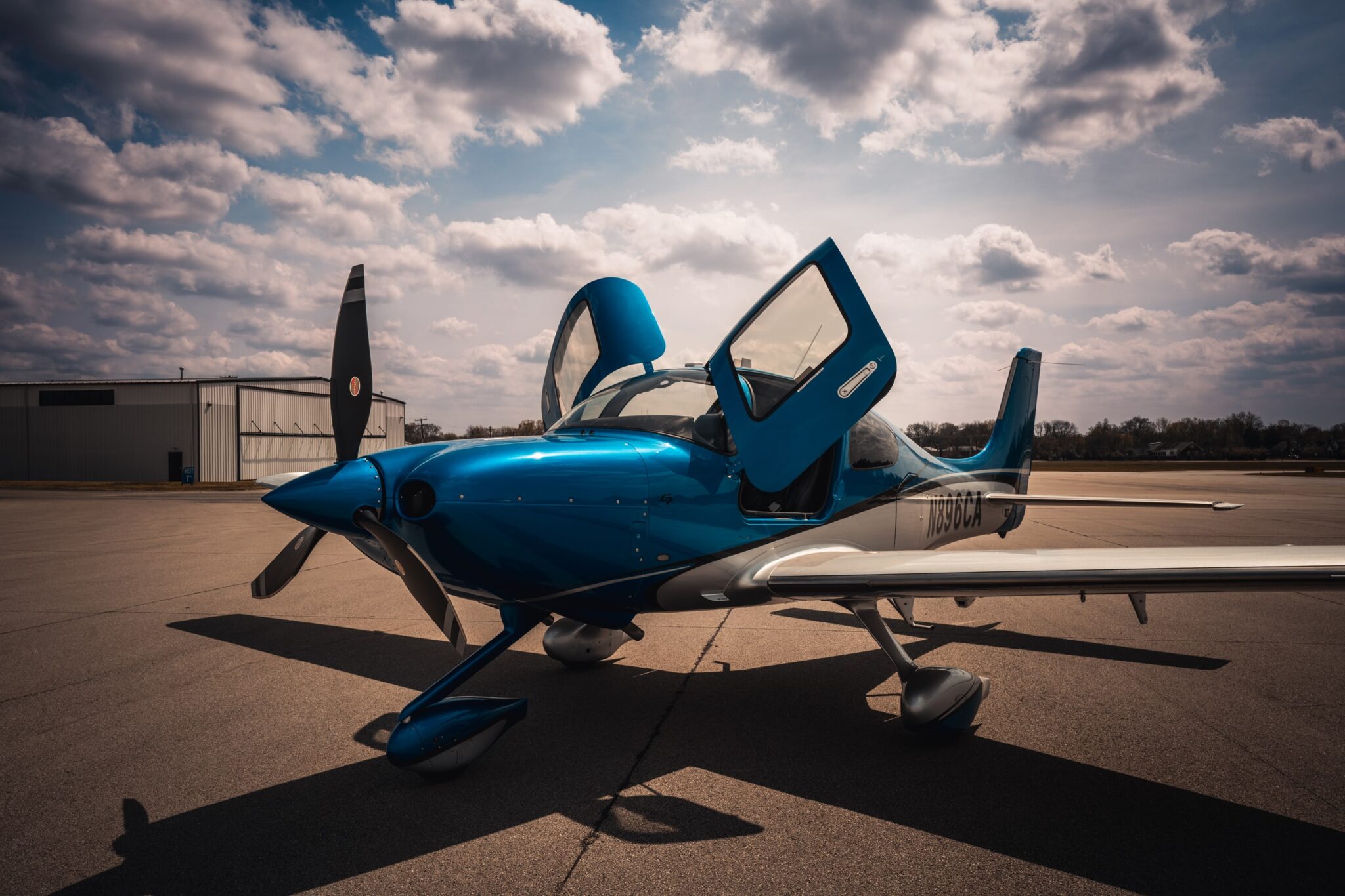 Blue Cirrus with doors open under a dramatic sky at Bowman Field