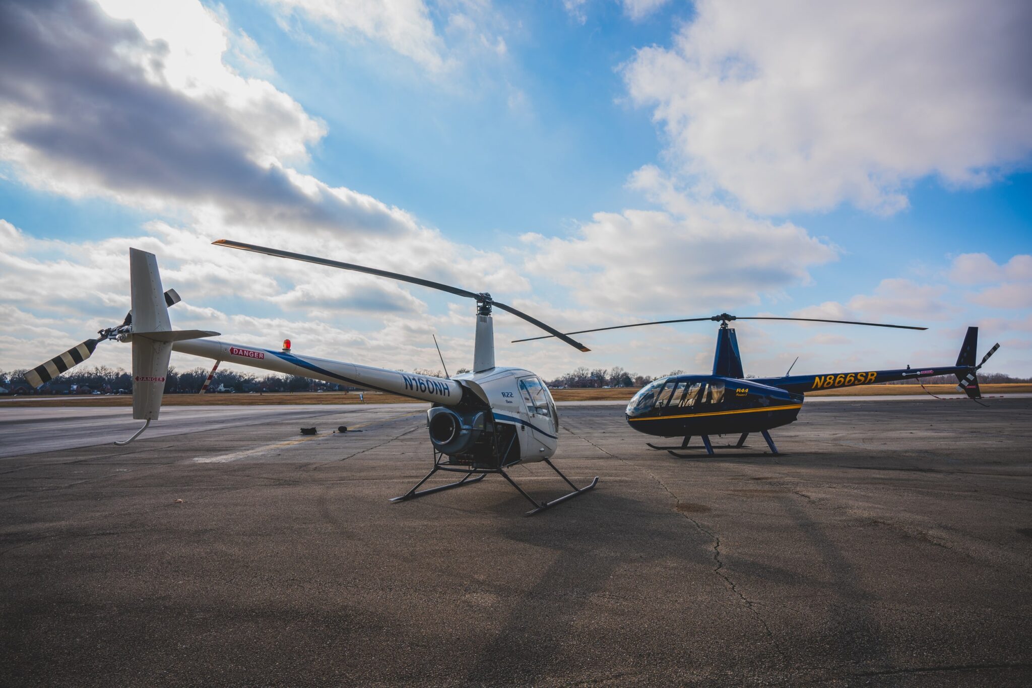Two Robinson helicopters on the ramp under a dramatic sky at Bowman Field