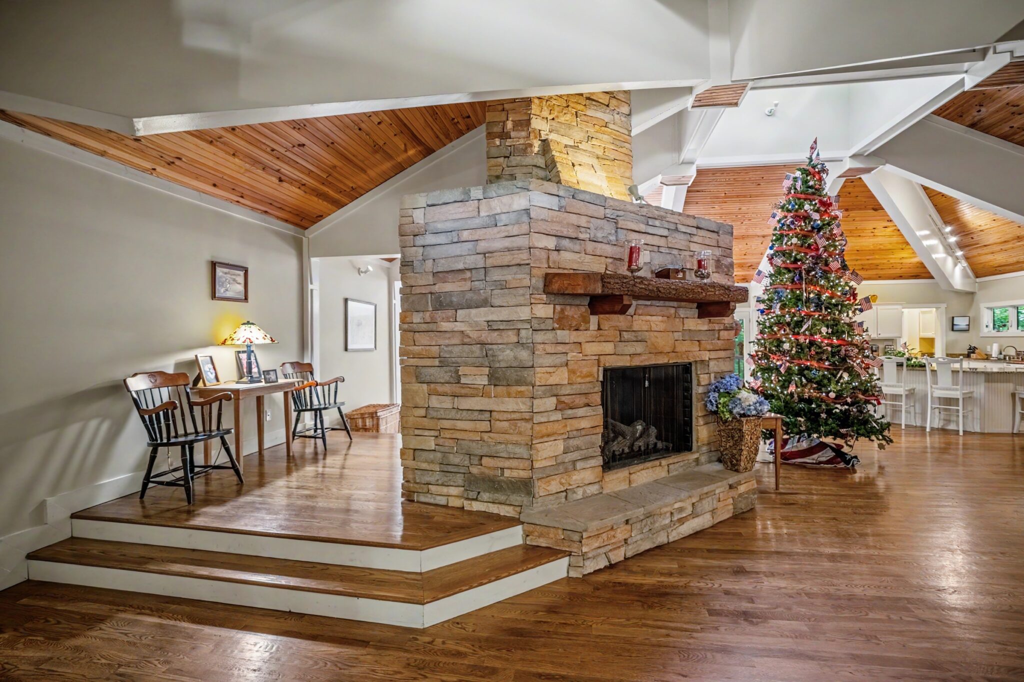 Great room with stacked-stone double-sided fireplace and vaulted wood ceiling, luxury lake house listing photography