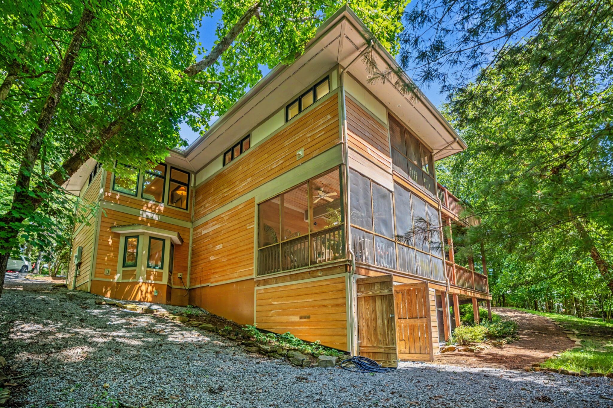 Cedar lake house exterior with two-story screened porch among the trees, real estate photography