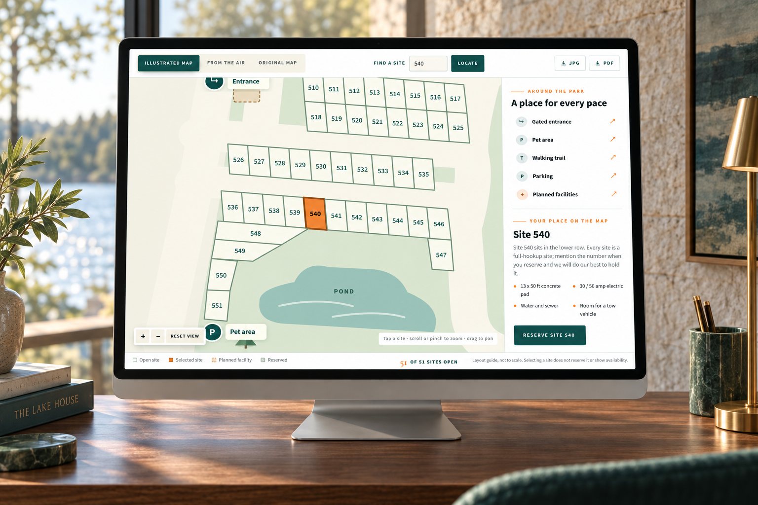 The Lakeside Oasis interactive park map with site 540 selected, on a desktop monitor in a lake-house studio, a presentation scene built from the real site.